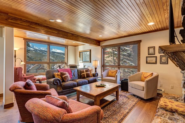 Spacious living room with wood ceiling, multiple seating areas, mountain views through large windows, and wood coffee table.